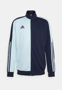 Marinblå och ljusblå zip-up träningsjacka med hög krage, med tre vita ränder på ärmarna och en Adidas-logotyp på bröstet.