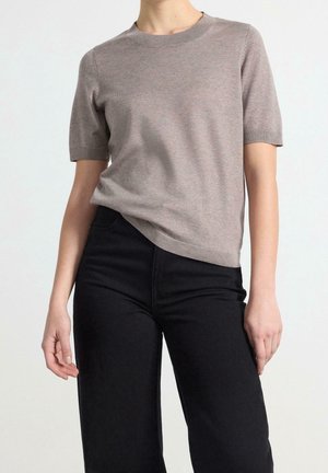 Jasnoszary dzianinowy sweter z krótkimi rękawami i okrągłym dekoltem, zestawiony z czarnymi spodniami z wysokim stanem. Gładka tekstura z minimalnymi zdobieniami.