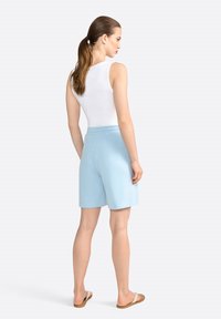 Shorts bleu clair avec une taille élastique, texture lisse et design jusqu'aux genoux, associés à un débardeur blanc et des tongs.