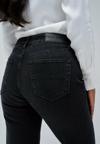 Černé džíny z denimu s obepínajícím střihem, na kterých je kožený štítek Salsa Jeans na pase a dvě zadní kapsy.