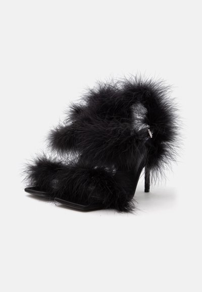 Sandales noires à talons hauts avec garniture en plumes duveteuses sur les brides et la cheville, présentées sur un fond clair uni.
