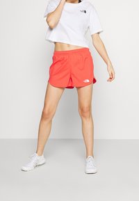 Röda sportshorts med elastisk midja, tillsammans med en vit kortärmad t-shirt med en liten logotyp och vita träningsskor.