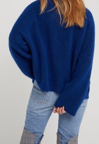 Blaues Wollmischung übergroßes Sweatshirt mit langen Ärmeln, strukturiertem Finish und cropped Saum, kombiniert mit hellblauen Jeans im Patchwork-Design.