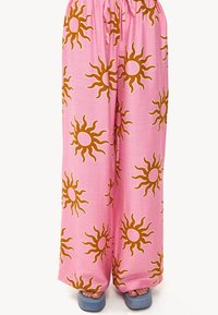 Pantalon large rose clair avec un motif de soleil en orange foncé. Tissu doux avec une taille élastique et une coupe décontractée.