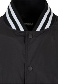 Czarna kurtka bomberka z czarno-białym prążkowanym ściągaczem przy kołnierzu, zapinana na zatrzaski, o gładkiej teksturze tkaniny.