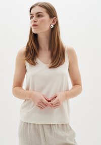 Heledbeez sleeveless top V-kaeluse disainiga, valmistatud siledast kangast; kantud heledate linased püksid, näidates lõdvat istuvust.