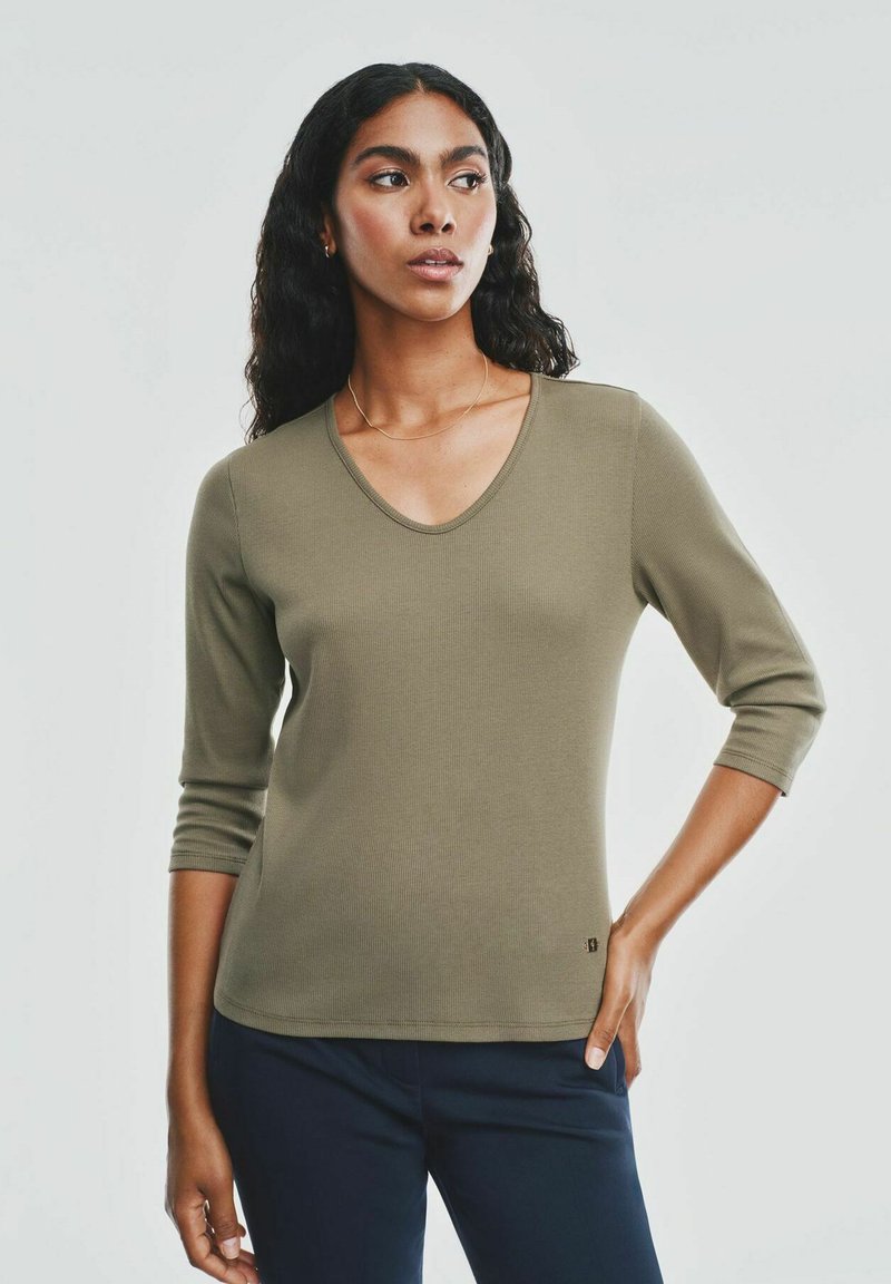 Oliwkowa, żeberkowana bluzka z długim rękawem i dekoltem w kształcie litery V, dopasowana, w zestawieniu z ciemnymi spodniami, ukazująca gładką teksturę.