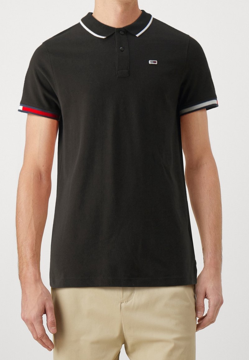 Czarna koszulka polo z białym kołnierzykiem, trzema guzikami z przodu oraz rękawami w blokach kolorystycznych z czerwonymi, niebieskimi i białymi akcentami.