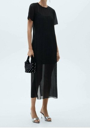 Personne portant une robe midi noire transparente à manches courtes, tenant un petit sac à main noir clouté et portant des talons ouverts argentés.