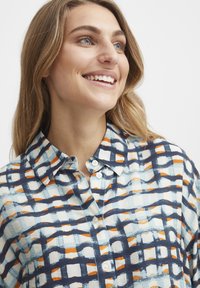 Camisa abotonada con un patrón de cuadrícula en marino, naranja y azul claro. Fabricada con una tela ligera y con un cuello estructurado.