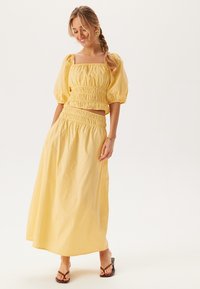 Twee-delig outfit bestaande uit een gele cropped top met smock en pofmouwen, en een bijpassende smock maxi rok, gemaakt van lichtgewicht stof.