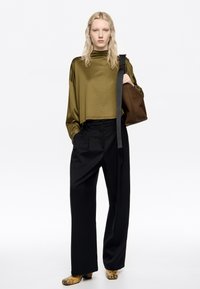 Olive green, krótka bluzka z długim rękawem; czarne spodnie z wysokim stanem; brązowa torba na ramię; wzorzyste żółte i czarne botki do kostki.