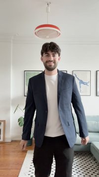 Navy blazer with two pockets, worn over a white shirt and black pants. Smooth fabric, tailored fit, displayed in a bright indoor setting.