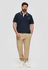 Marineblauw poloshirt met witte accenten en kraag, gecombineerd met beige broek met trekkoord en witte sneakers. Casual, comfortabele pasvorm en ontwerp.