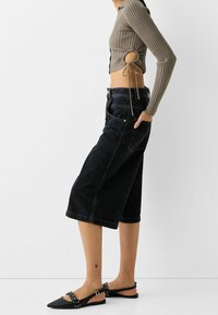 Black denim culottes with a loose fit, complemented by a brown ribbed knit top featuring side cutouts and ties, paired with flat black shoes.