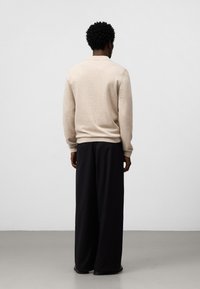 Maglione beige con polsini a costine, vista posteriore. Abbinato a pantaloni neri a gamba larga. Tessuto morbido, vestibilità casual, dettaglio del colletto sottile.