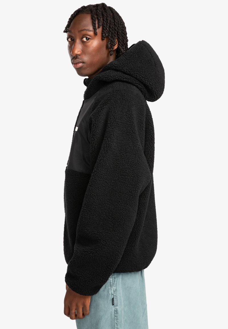 Pullover in pile nero con cappuccio, dotato di un pannello in contrasto nero sulla parte anteriore. Texture morbida e design allentato.