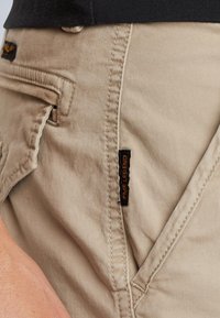 Beige cotton shorts with dual side pockets, tonal stitching, and a black label displaying "Prime Legend" on the front pocket.