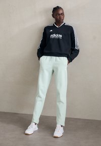 Zwarte sweatshirt met witte 'adidas' logo en drie strepen op de mouwen; mintgroene broek; witte sneakers met gestructureerde accenten.
