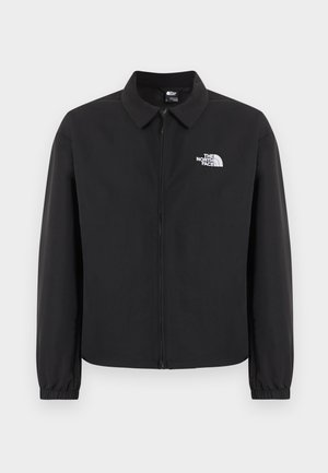 Geacă neagră cu fermoar frontal, guler, manșete elastice și logo alb The North Face pe pieptul stâng, afișată pe un fundal simplu.