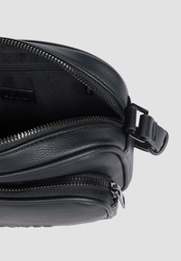 Schwarze Leder-Crossbody-Tasche mit strukturiertem Design, doppelten Reißverschlussfächern und elegantem Metallzubehör. Verfügt über ein strukturiertes Material und einen verstellbaren Tragegurt.