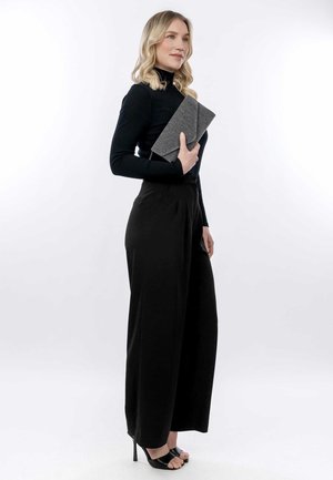 Top lungo nero a coste, pantaloni neri a vita alta e larghi, con una clutch grigia texture, completati da sandali neri con tacco.
