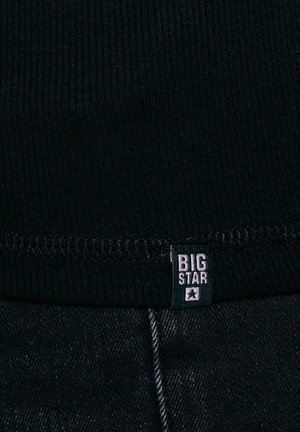 Fekete bordázott szövet varrott szegéllyel, felette egy kis fekete címke "BIG STAR" felirattal, sötét farmernadrág fölött.