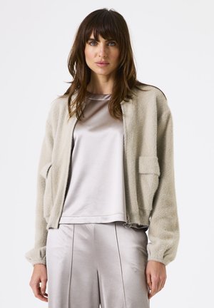 Fleece jack met een lichte grijze kleur, met een ritssluiting aan de voorkant, verlaagde schouders, twee zakken en geribbelde manchetten. Ggedragen over een satijnen top en zijden broek.