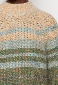 Sweter dziany z wysokim kołnierzem, z wielokolorowym wzorem w odcieniach beżu, niebieskiego i zielonego, prezentujący różnorodne tekstury włóczki.