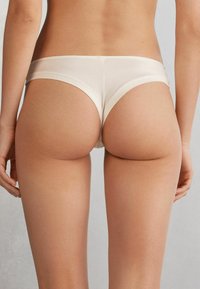 Beige fabric hipster panties with a smooth texture, low-rise design, and wide elastic band along the waist, viewed from the back.