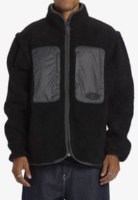 Svart fleecejacka med grå nylon detaljer och dragkedjefickor. Har en hög krage och elastiska ärmslut. Mjuk textur och avslappnad passform.