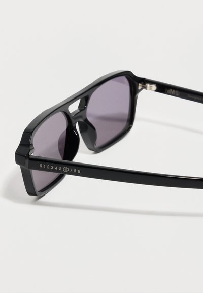 Μαύρα ορθογώνια γυαλιά ηλίου με σκουρόχρωμους φακούς, που φέρουν έναν αριθμητικό λογότυπο τυπωμένο στο μπράτσο του κτυπητού κατα μήκος ενός λευκού φόντου.