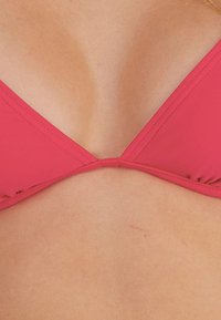 Rosa Bikini-Oberteil mit V-Ausschnitt, dreieckigen Körbchen und sauberer Naht. Das Material hat eine glatte Textur mit minimalen Akzenten.