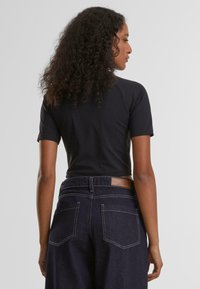 Svart tettsittende t-skjorte med korte ermer, brukt sammen med høy midje blå denimjeans med en brun lærlapp bak.