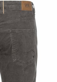 Grijze corduroy broek met een leren merkpatch op de tailleband en een achterzak met een gestikt ontwerp. Getextureerde stof met verticale ribbels.