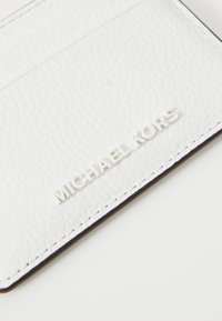 Witte gestructureerde leren kaarthouder met debossed "MICHAEL KORS" logo. Eenvoudig, compact ontwerp met scherpe randen en contrasterende stiksels.