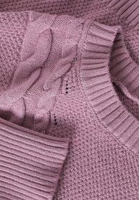 Pull en maille mauve avec des motifs torsadés en câble et en point de semence, col et poignets côtelés.