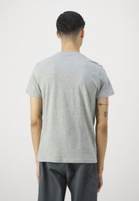 Kortermet grå t-skjorte laget av mykt stoff, med klassisk rund hals og avslappet passform, sett fra ryggen. Viser en tatovering på armen.
