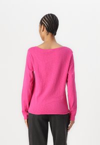 Långärmad rosa topp med avslappnad passform, rund halsringning och ribbade ärmslut, tillsammans med mörka byxor. Slät textur, avslappnad design.