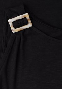 Tissu noir avec une boucle rectangulaire en écaille sur une sangle, montrant la texture et les coutures en gros plan.