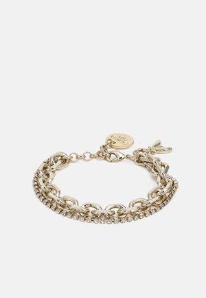 Bransoletka na łańcuszku w odcieniu złota z jasną linią kryształków, zapięciem na karabińczyk i małą okrągłą przywieszką z wyrytym tekstem na białym tle.