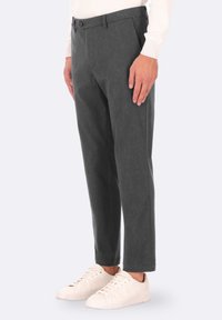 Pantaloni grigi a righe, dal taglio tailored, con chiusura a bottone e una lieve texture, abbinati a sneakers bianche.
