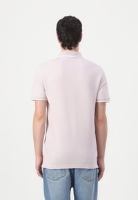 Polo shirt rose clair avec un contraste blanc sur le col et les manches, fabriqué en tissu doux, associé à un jean bleu clair.