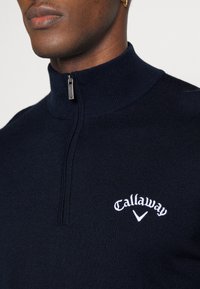 Navy blue zip-up sweater with high collar, made of a ribbed fabric featuring white embroidered "Callaway" logo on the chest.