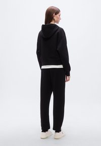 Μαύρο κοντό φούτερ με κουκούλα, με μακριά μανίκια. Συνδυασμένο με μαύρο παντελόνι jogger και ανοιχτόχρωμα αθλητικά παπούτσια. Ομαλή υφή υφάσματος.