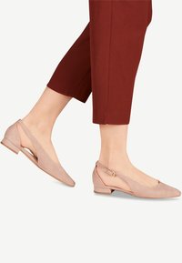 Bailarinas de talón abierto en suave ante rosa claro con un tacón bajo, punta afilada y detalles laterales cortados asegurados con una pequeña hebilla ajustable.