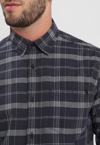 Granatowa koszula w kratę z bawełny z białymi paskami, zapinana na guziki, z kołnierzykiem button-down i kieszenią na piersi, charakteryzująca się klasycznym wzorem w kratę.