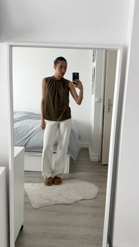 Olive green sleeveless top with a gathered neckline, paired with white wide-leg pants and brown slippers, standing in a bedroom.