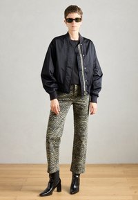 Crna bomber jakna s rebrastim manžetama, kombinirana s maslinasto zelenim hlačama koje imaju valoviti uzorak. Završava s crnim čizmama na visoku petu.