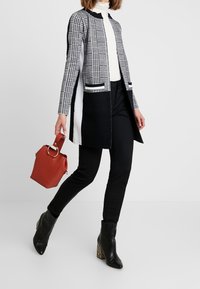Abrigo largo de cuadros en blanco y negro con cuello redondeado, corte ajustado y aberturas laterales, combinado con pantalones negros y botas negras con estampado de serpiente.